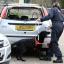 A sniffer dog is worked around a burned out car at the scene of a fire in Harlow, Essex, where a woman and four children died after a house fire