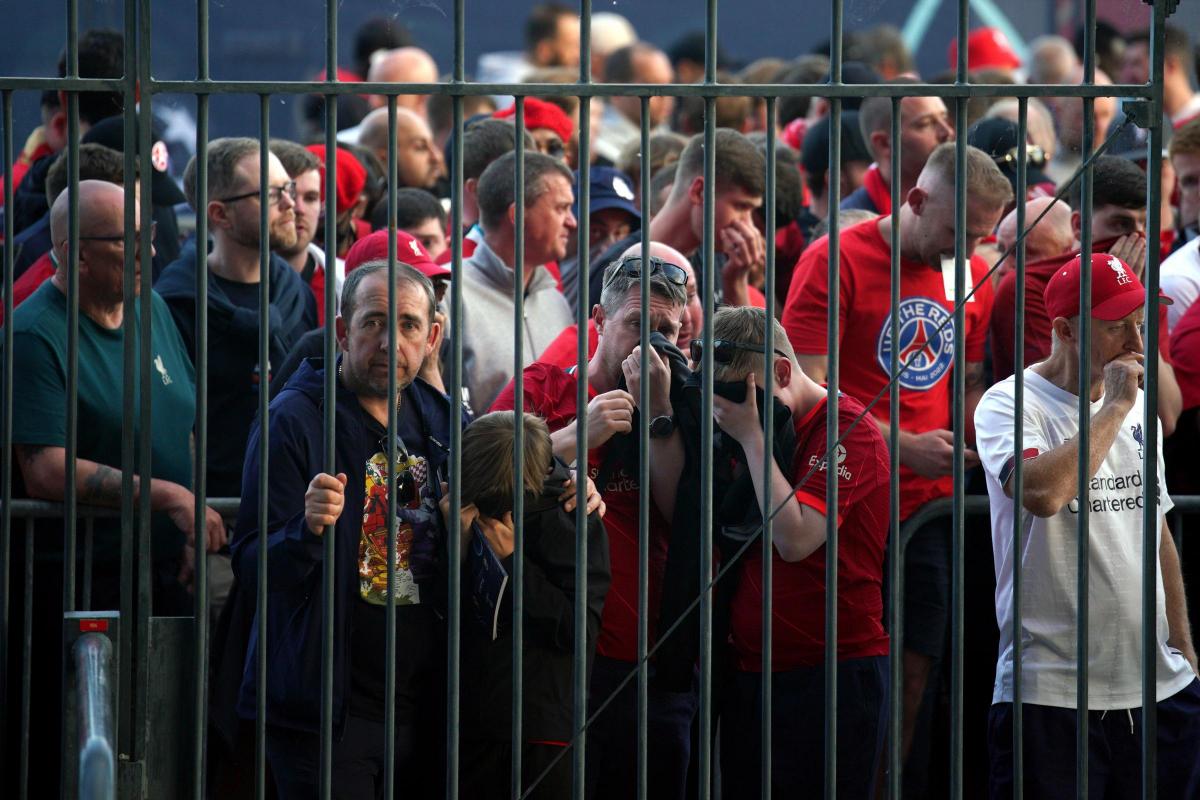 Liverpool fans cover their mouths and noses as they queue to gain entry to the Stade de France